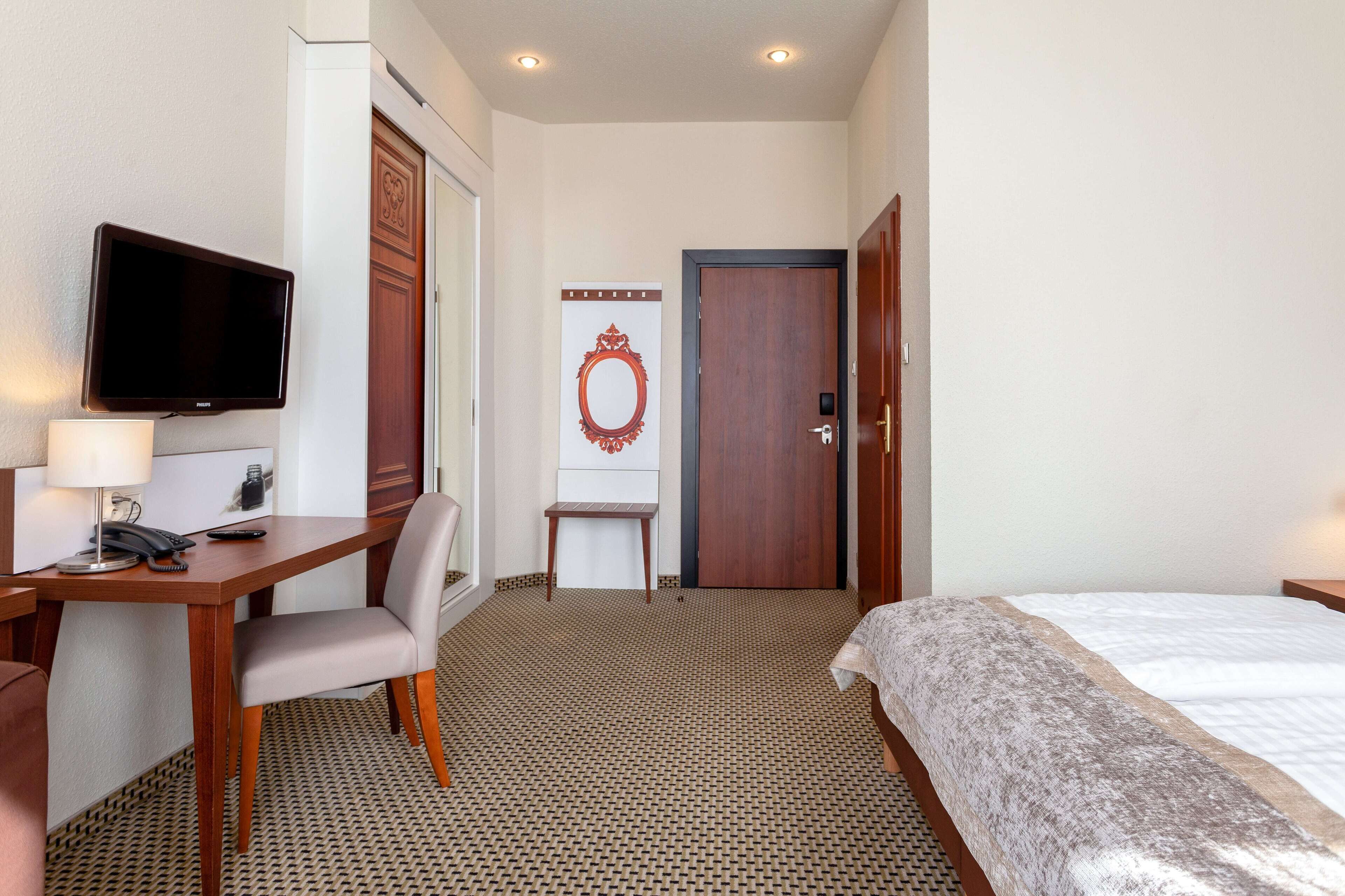 Une chambre d’hôtel comprenant un lit, un bureau avec une chaise, une télévision et un miroir.