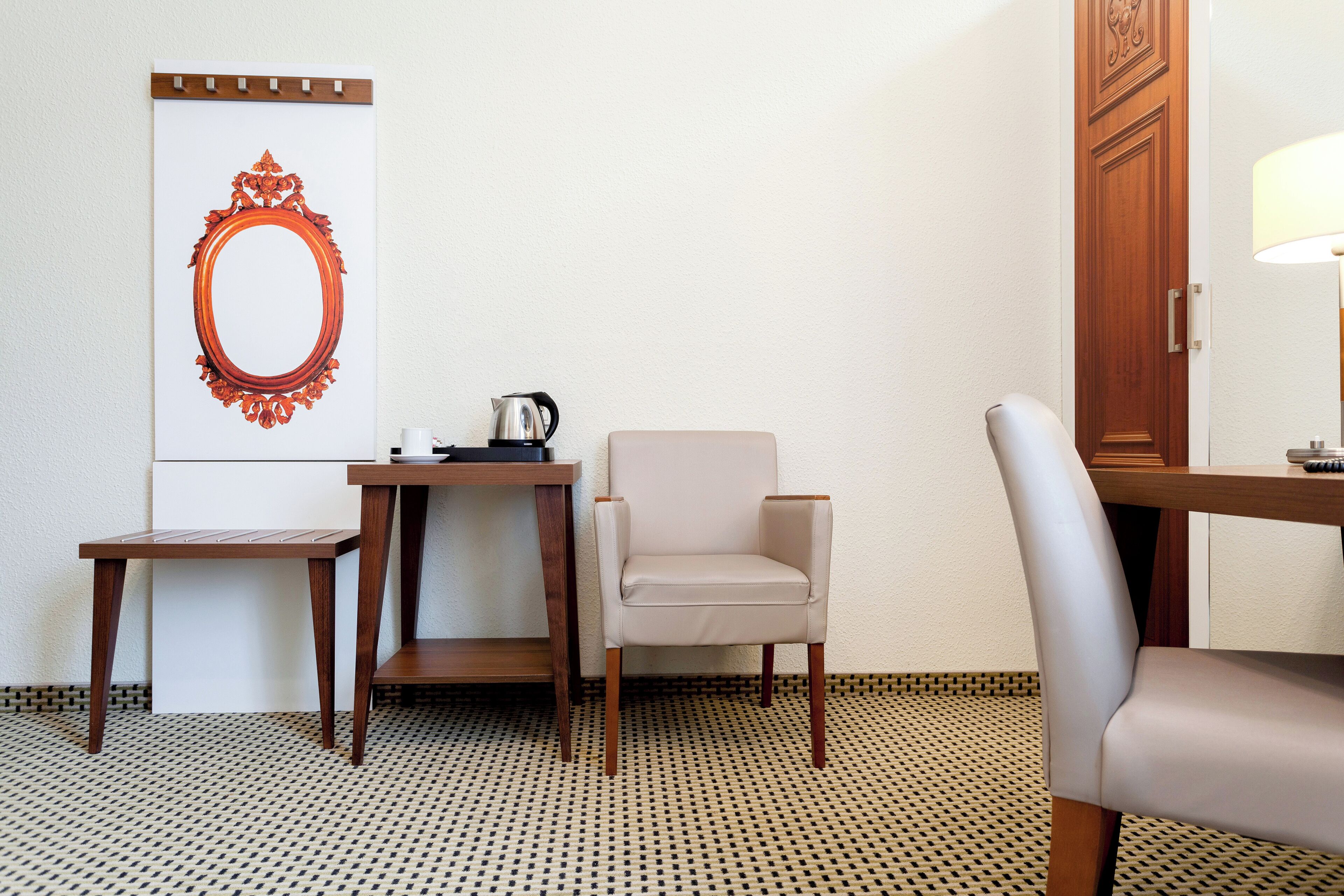 Habitación de hotel con suelo de madera, una mesita con hervidor, una silla y un espejo grande en la pared.