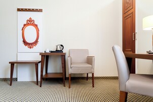 Habitación de hotel con suelo de madera, una mesita con hervidor, una silla y un espejo grande en la pared.