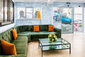 Een ontvangstgebied met een groene hoekbank, een glazen salontafel en een decoratieve bloemstelling.