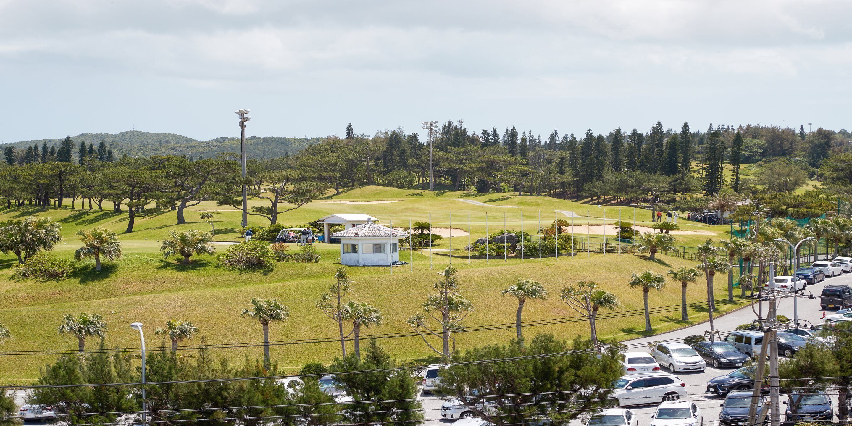 A golf course with a clubhouse, palm trees, and a parking lot.