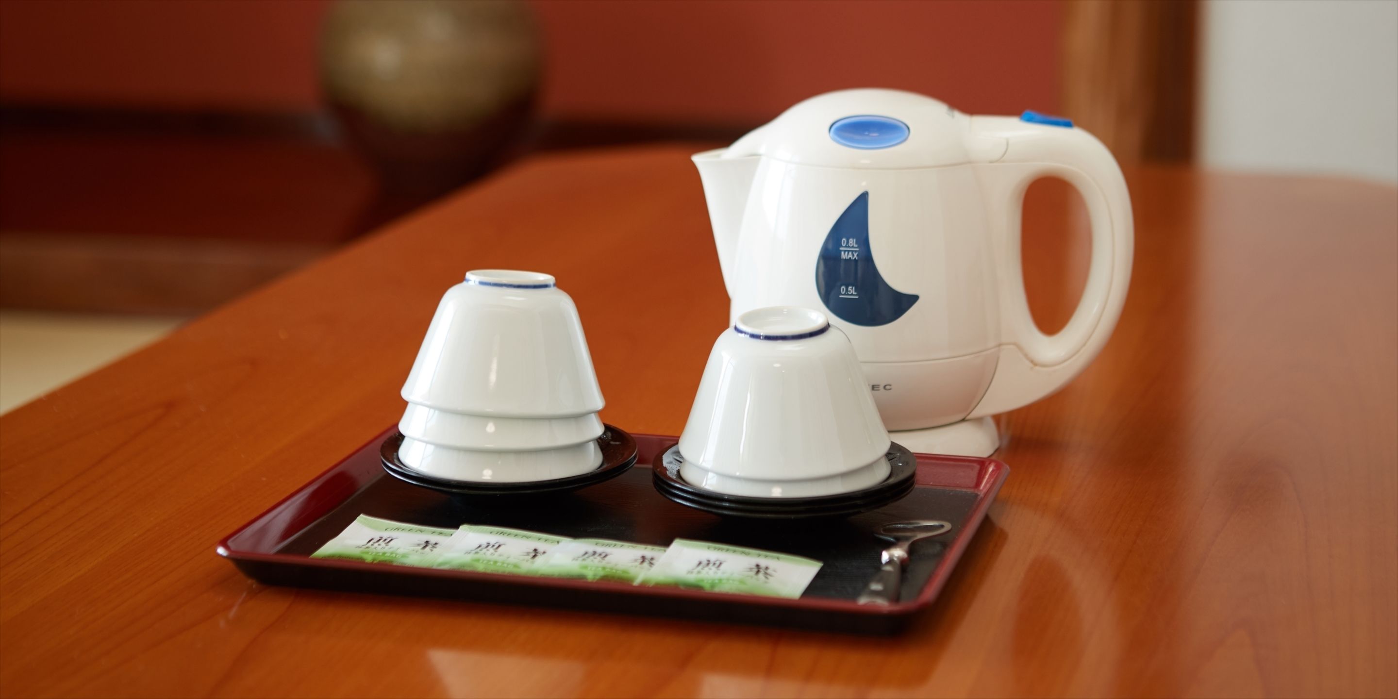 A white electric kettle with a blue label on a tray with two white cups and a tea bag.