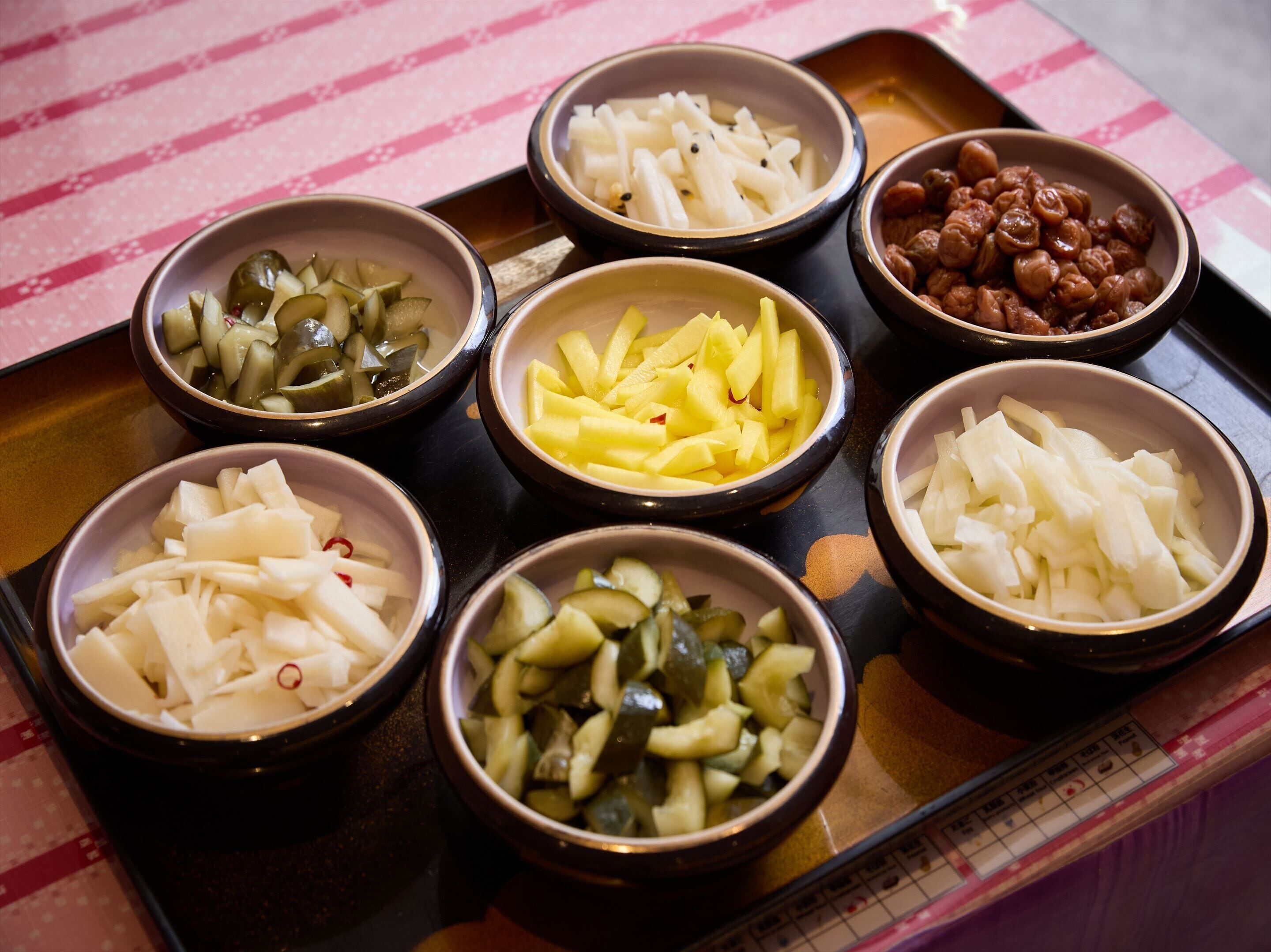 A tray with bowls containing various pickled vegetables and fruits.