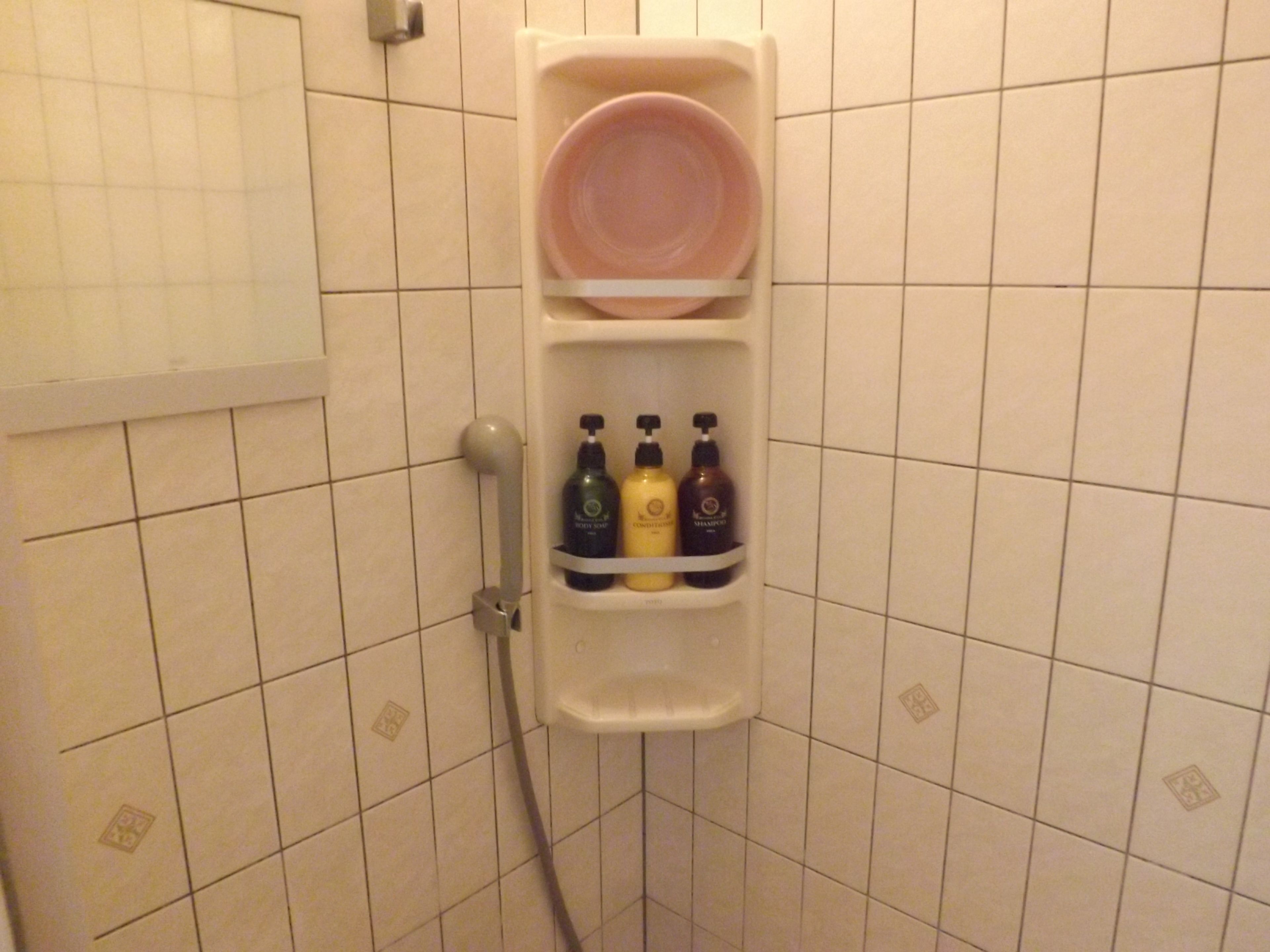 A bathroom with a white tiled wall, a shower area, and a shelf with toiletries.