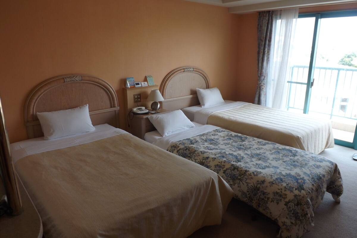 A hotel room with two single beds, a nightstand with a lamp, and a window with curtains.