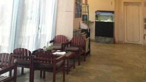 A spacious lobby with a high ceiling, a seating area with wooden chairs and tables, a fish tank, and a reception desk. - Hotel Bell Harmony Ishigakiisland (Ishigaki)