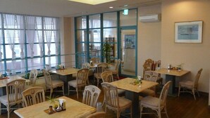 A dining area with multiple tables and chairs, large windows, and an air conditioning unit on the wall. - Hotel Bell Harmony Ishigakiisland (Ishigaki)