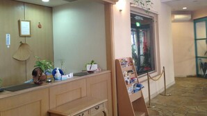 A reception area with a wooden desk, a framed certificate, and a small plant. - Hotel Bell Harmony Ishigakiisland (Ishigaki)