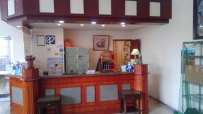 A reception desk with a wooden finish, a framed picture on the wall, and a green cabinet. - Hotel Peace Land Ishigakijima (Ishigaki)