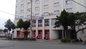 A multi-story building with a sign indicating a hotel. There are trees in front, and a few scooters parked outside.