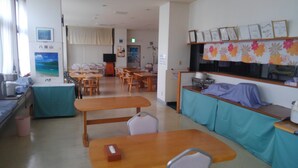 A room with multiple wooden tables and chairs, a sofa, a counter with a sink, and a window with curtains.