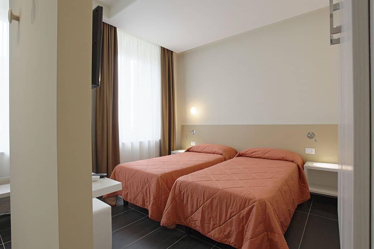Ein Hotelzimmer mit zwei Betten, einem Nachttisch, Vorhängen an einem Fenster und einer Wandleuchte.
