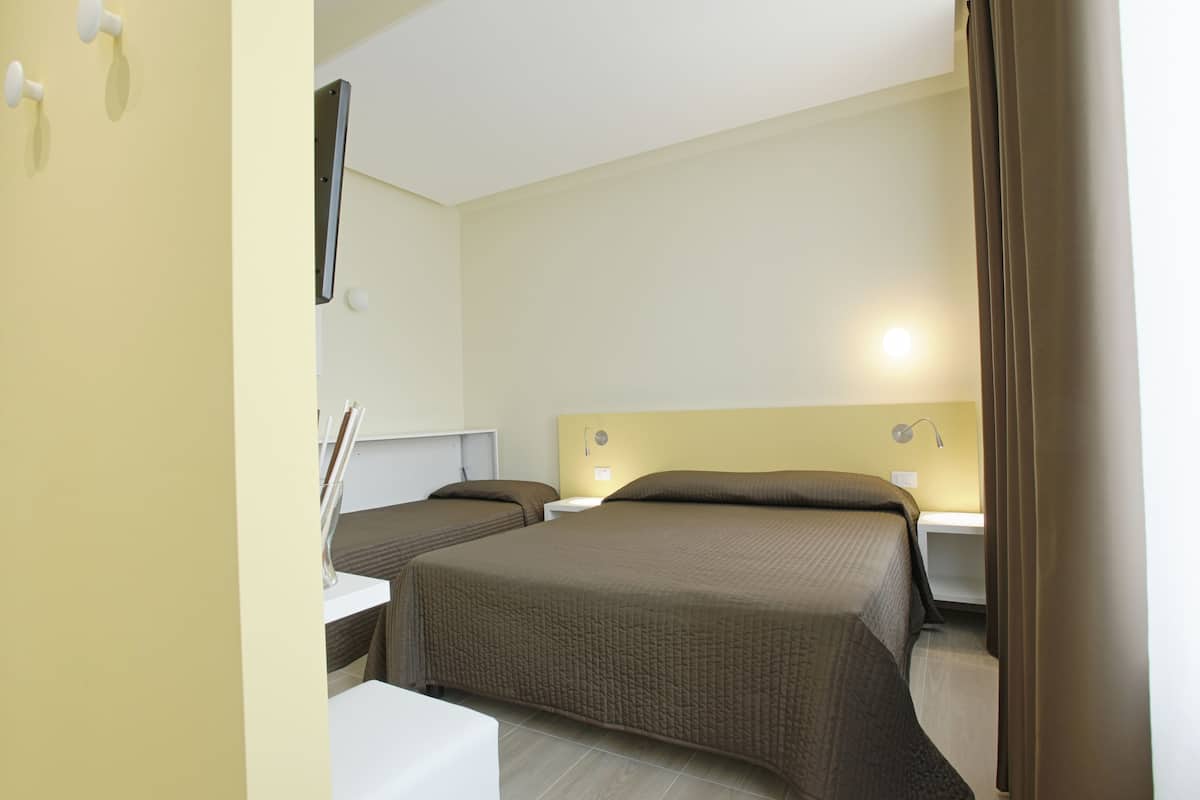 Ein Hotelzimmer mit zwei Betten, einem Schreibtisch und einem an der Wand montierten Fernseher.