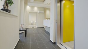 A modern hallway with a reception desk, a potted plant, and a bright yellow door. - Hotel Agrigento Home (Agrigento)