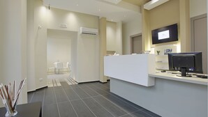 A modern reception area with a reception desk, a flat-screen TV, and a seating area with tables and chairs. - Hotel Agrigento Home (Agrigento)