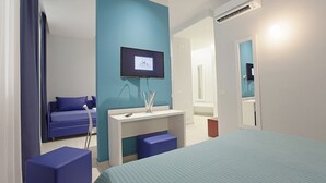 A modern hotel room with a large bed, a TV, a desk, and a blue sofa. - Hotel Agrigento Home (Agrigento)