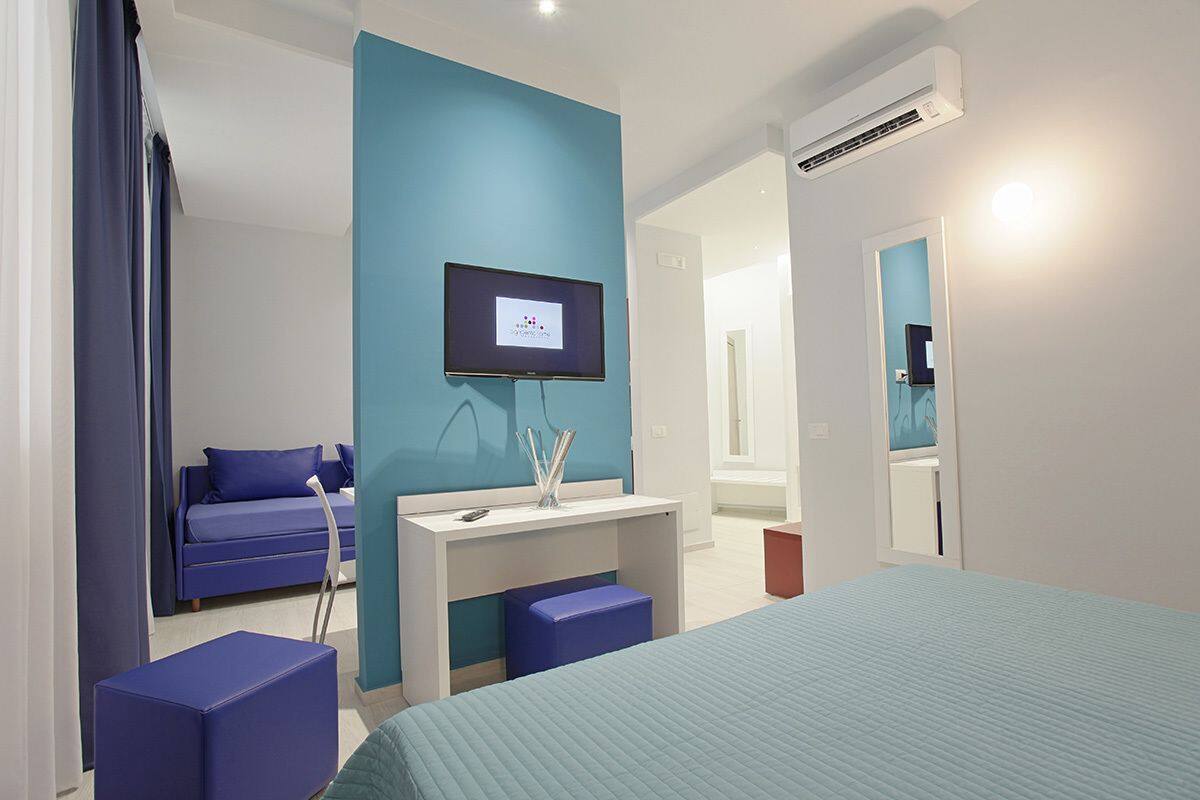 Ein modernes Hotelzimmer mit einem großen Bett, einem Fernseher, einem Schreibtisch und einem blauen Sofa.