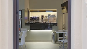 A compact bar area with a coffee machine, shelves with bottles, and a trash bin. - Hotel Agrigento Home (Agrigento)