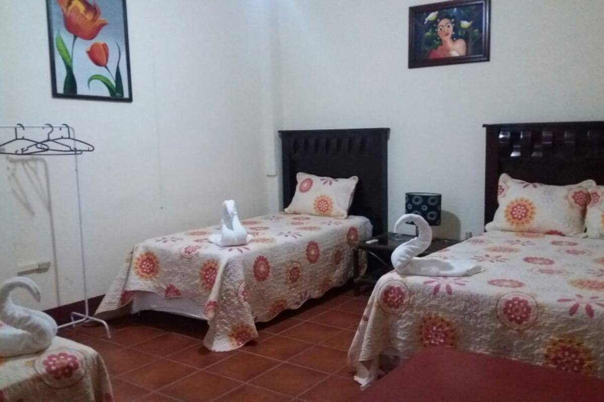 Ein Schlafzimmer mit zwei Betten, jeweils mit floraler Bettwäsche und dekorativen Schwanenkissen. An der Wand befinden sich Wandhaken und ein gerahmtes Bild.