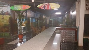 A hallway with a long table, chairs, potted plants, and colorful murals on the walls. - HOTEL & CASINO ATLANTIC CITY de SAN JUAN DEL SUR (San Juan del Sur)