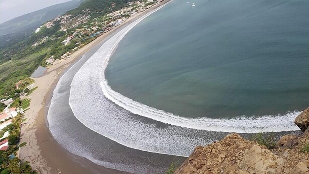 A coastal landscape with a curved beach, rocky shoreline, and a backdrop of hills and buildings. - HOTEL & CASINO ATLANTIC CITY de SAN JUAN DEL SUR (San Juan del Sur)