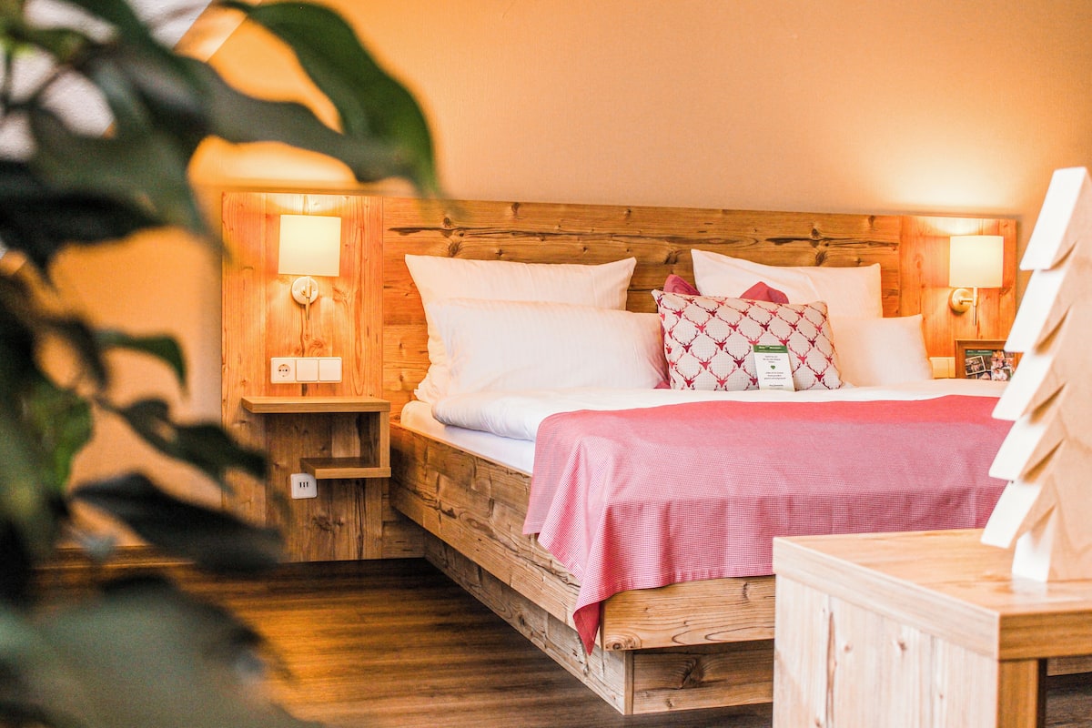 A wooden bed with white and patterned pillows, a pink bedspread, and two bedside lamps.