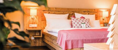 Una cama de madera con almohadas blancas y estampadas, una colcha rosa y dos lámparas de noche.