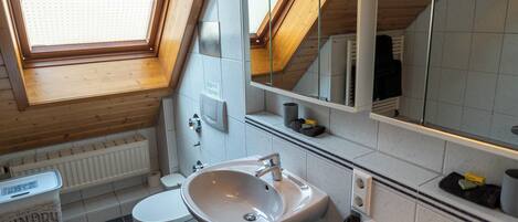 Un baño moderno con tragaluz, un espejo grande y un lavabo blanco.