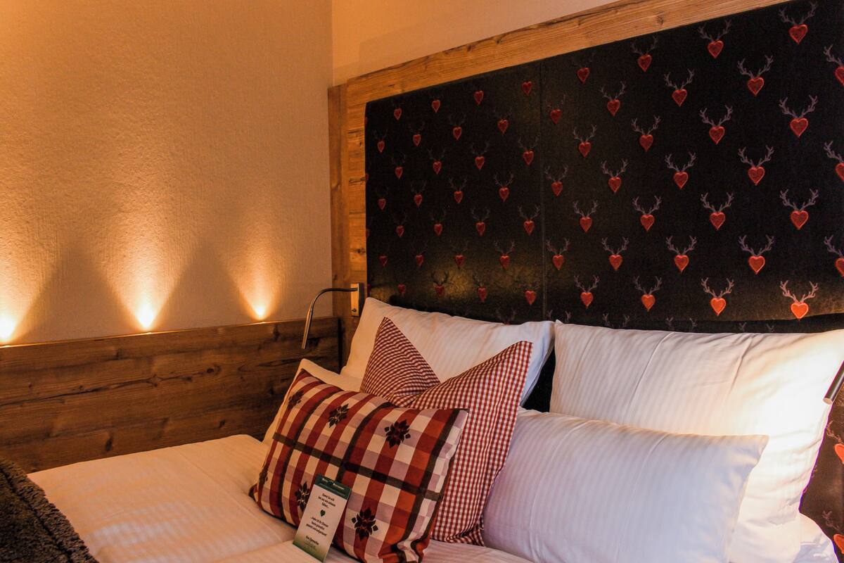 A bed with white and red checkered pillows, a wooden headboard, and a wall with a heart pattern.