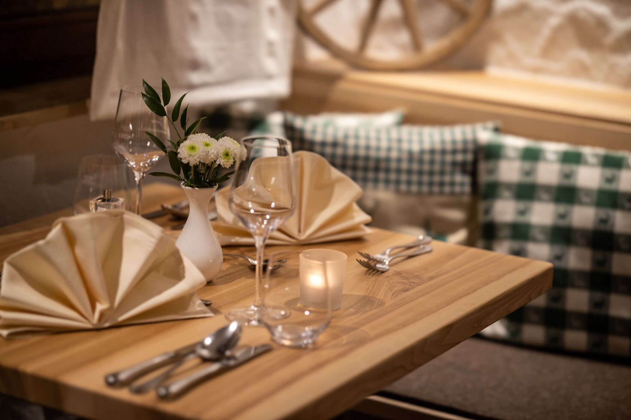 Een houten eettafel gedekt met witte servetten, bestek, wijnkannen en een kaars.