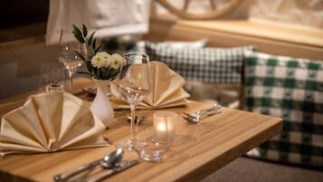 Een houten eettafel gedekt met witte servetten, bestek, wijnkannen en een kaars.