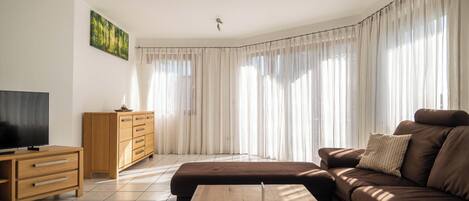 A living room with a brown sofa, a wooden coffee table, a TV on a wooden stand, and a cabinet.