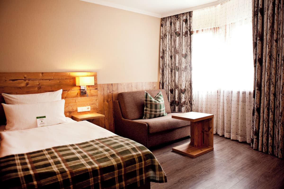 A hotel room with a bed, a sofa, a small wooden table, and a nightstand with a lamp.