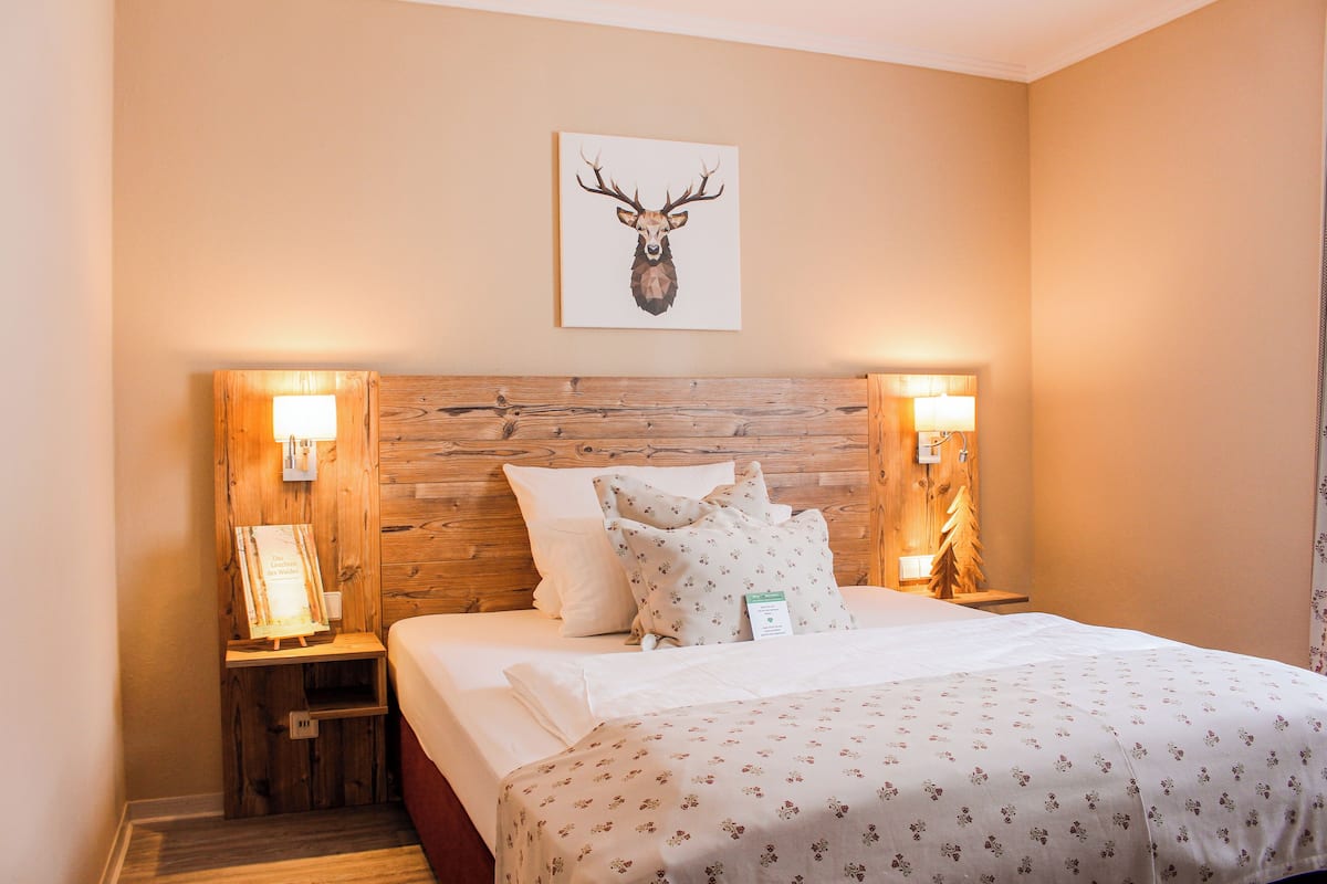 A hotel room with a wooden headboard, a bed with floral bedding, two bedside lamps, and a framed deer head artwork on the wall.