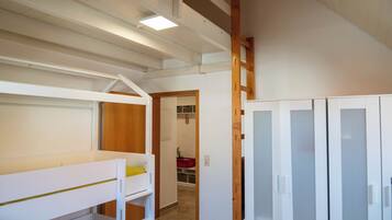 A room with a bunk bed, a wardrobe, and a door leading to a bathroom.