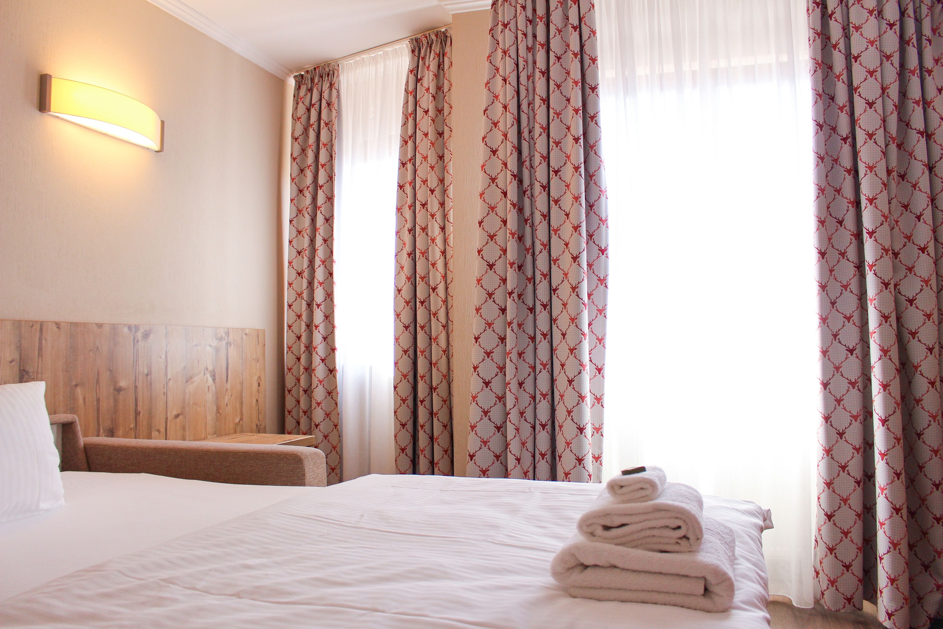 Una habitación de hotel con una cama bien hecha, un cabecero de madera y cortinas con estampado rojo.