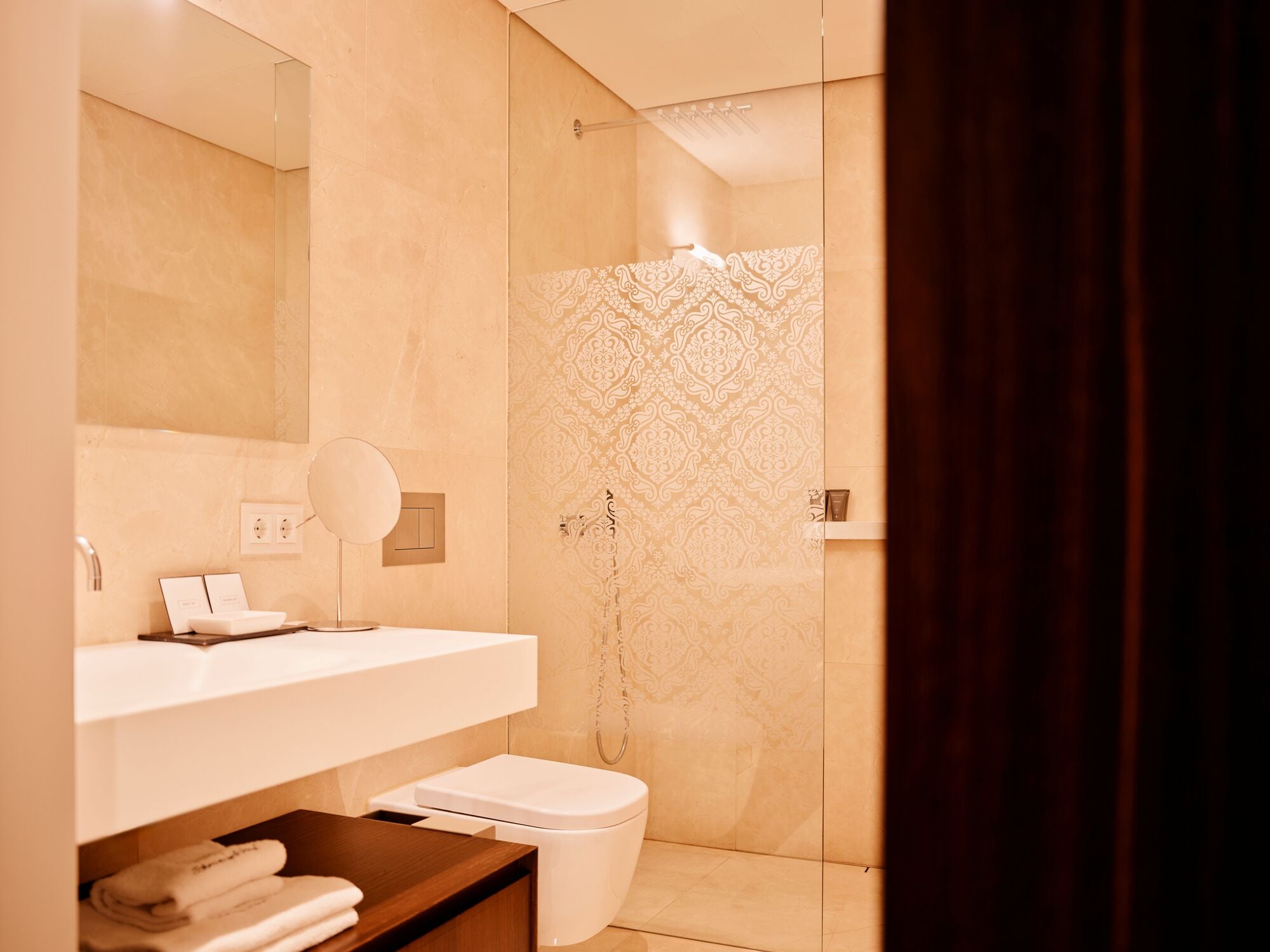 A modern bathroom with a glass shower enclosure, a white sink, and a wooden vanity.