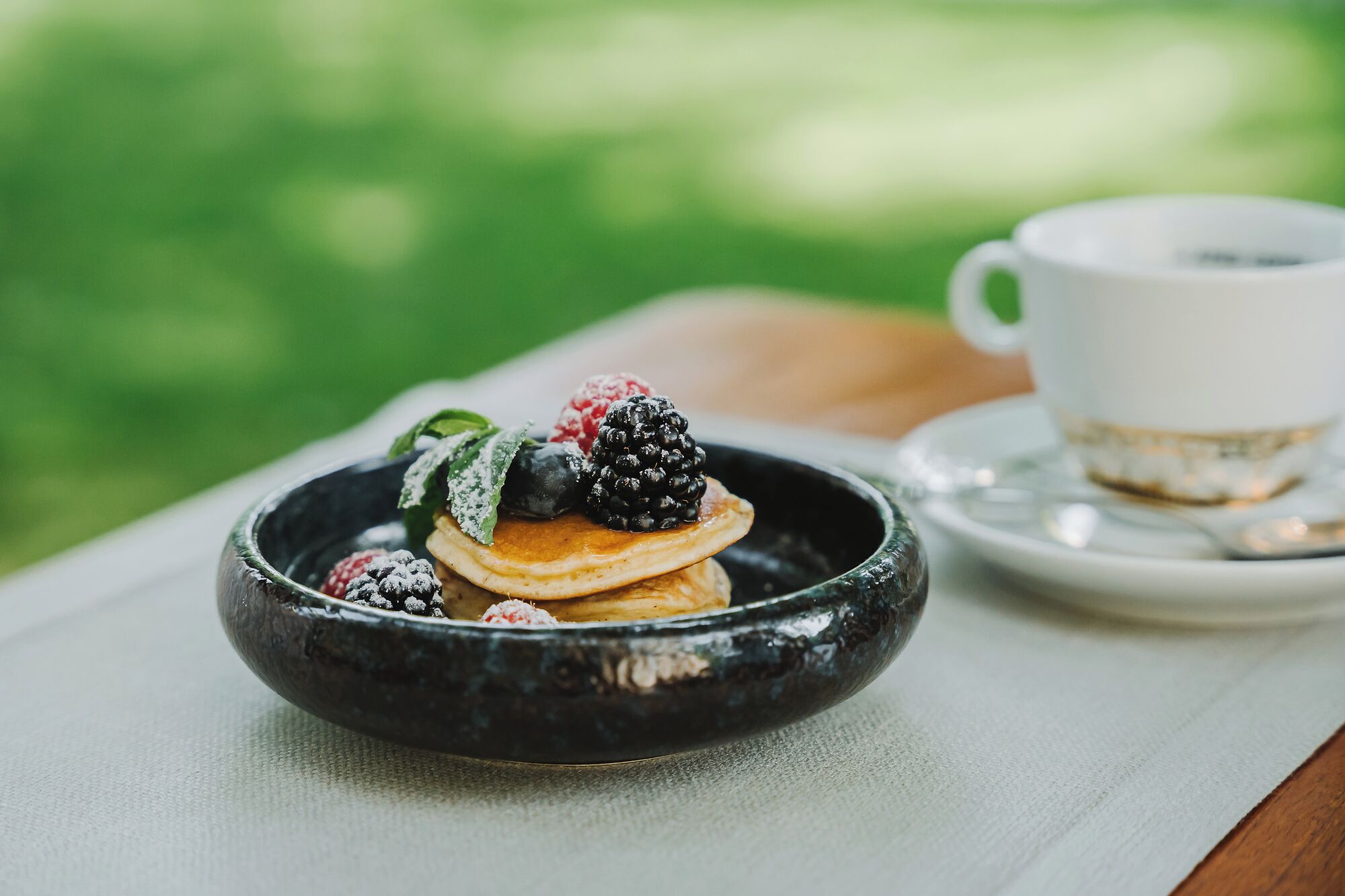 A breakfast setup with pancakes, berries, and a cup on a table.