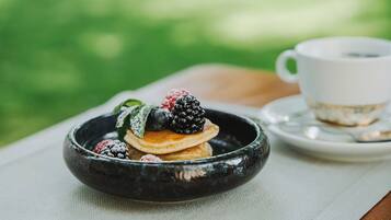 Ein Frühstückstisch mit Pfannkuchen, Beeren und einer Tasse.