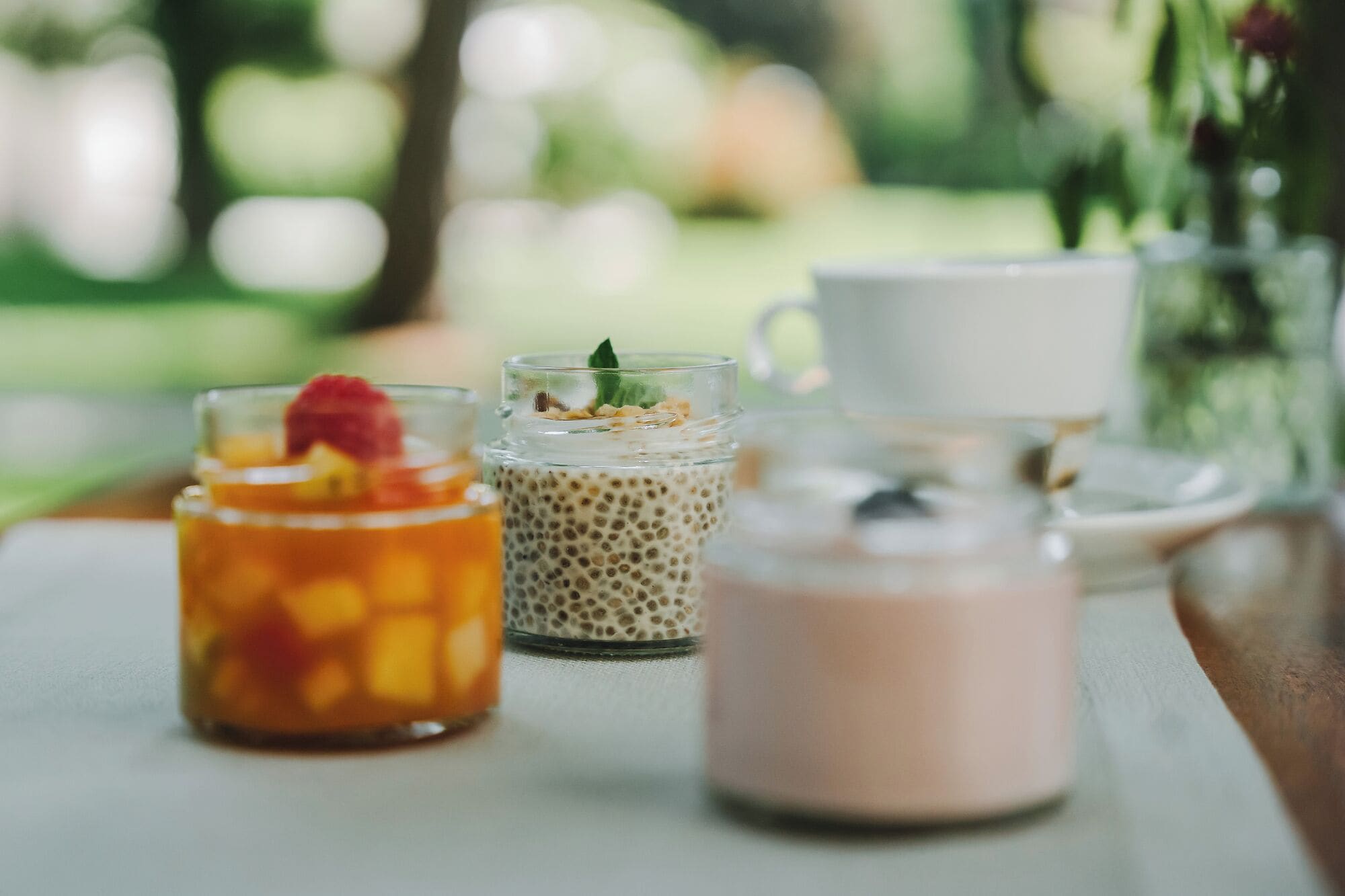 A table with three glass containers of different beverages and a white cup.