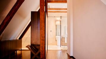 Un escalier en bois mène à une salle de bain équipée d’une douche et d’un miroir.