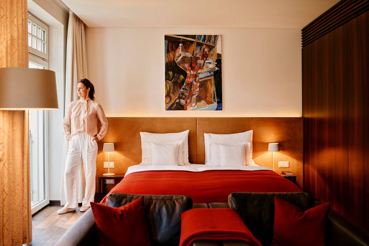A hotel room with a large bed, two bedside lamps, a painting on the wall, and a window with curtains.