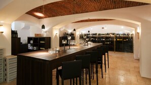 Zona de bar con barra de madera, varios vasos de vino y botellas en estantes.