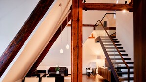 Un loft moderno con una escalera de madera, un comedor con mesa y sillas, y una zona de estar acogedora con sofá y una planta.