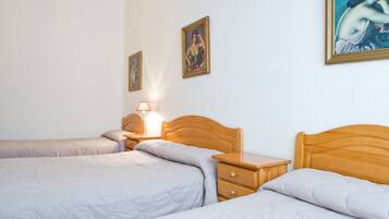 Habitación de hotel con dos camas individuales, una mesita de noche con lámpara y dos cuadros enmarcados en la pared.