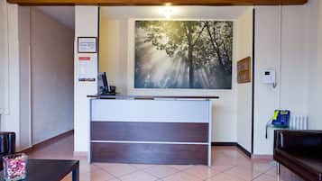 A reception desk with a computer, a framed certificate on the wall, and a painting of trees.
