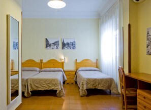 A room with two single beds, a wooden desk, and a chair. There are two wall-mounted lamps and three framed pictures on the wall. - Hostal América (Madrid)