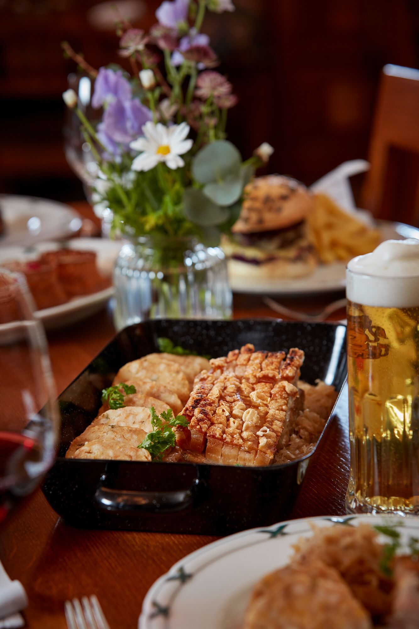 Taula de menjador amb un plat de carn a la graella, un got de cervesa i un ram de flors.