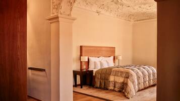 A bedroom with a wooden headboard, a bed with patterned bedding, a nightstand with a lamp, and a decorative ceiling.