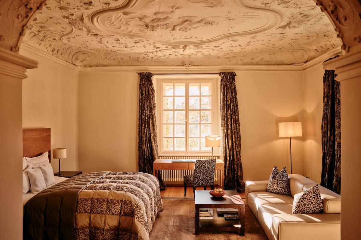 A room with a bed, a sofa, a table, and a window with curtains.